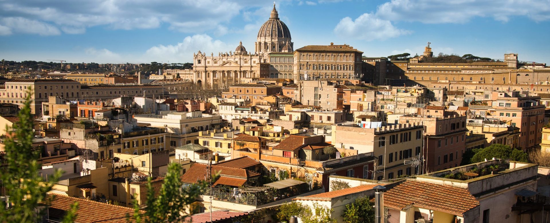 St. Peter's Basilica at daylight with cloudy blue sky. Buildings in foreground. Rome, Vatican, Italy